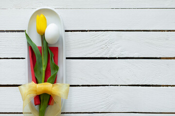 Egg and yellow tulip decorative aranged as mimal bouquet with bow on plate with white wooden background. Creative Easter idea and concept. Flat lay.