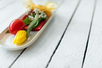 Red egg and yellow tulip decorative aranged as mimal bouquet with bow on plate with white wooden background. Creative Easter idea and concept. Flat lay.