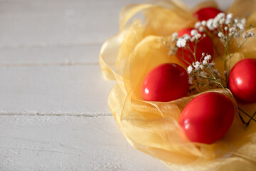 Red easter eggs decorative aranged with yelow ribbon as nest and whit tine flowers on wooden table.