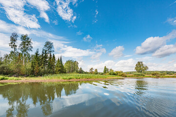 Obraz na płótnie Canvas Panoramic landscape on a sunny day on the river with the sky in the clouds and the reflection in the water.
