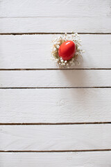 Red color Easter egg in nest with tine flower on white wooden table. Decorative minimal concept. Flat lay.