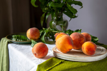 Peaches on table in kitchen near window. Rustic minimalism food peach fruits with leaves on wooden...