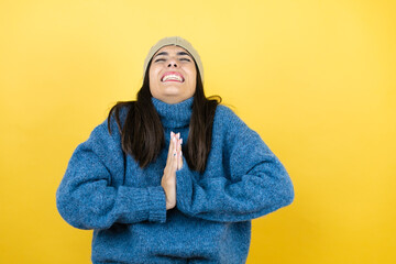 Young beautiful woman wearing blue casual sweater and wool hat begging and praying with hands together with hope expression on face very emotional and worried