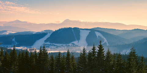 Obraz premium A Scenic view on a ski resort during a warm sunset in winter with a snowy mountain ridge in behind