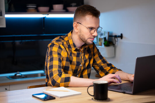 Portrait of male programmer in a yellow-black-gray shirt in a cage and glasses using Programs computer code in a Home. Works professionally on laptop. Concept programmer Day.