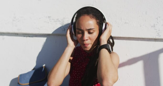 African american woman wearing headphones and listening to music on promenade by the sea