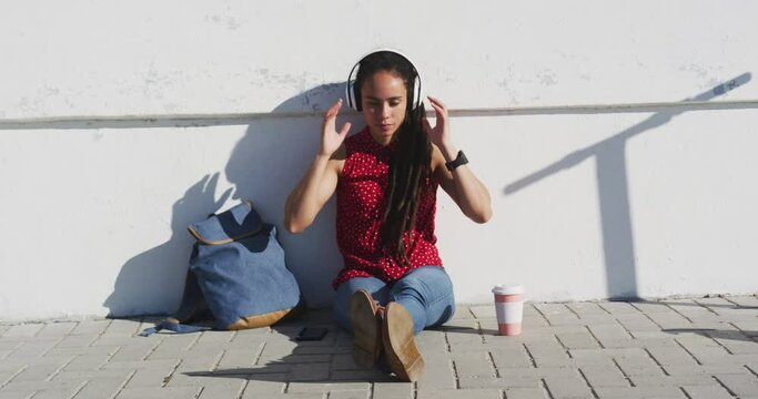 African american woman wearing headphones and listening to music on promenade by the sea