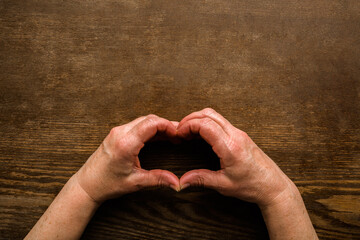 Heart shape created from mature woman hands on dark wooden table background. Love, health and hope...