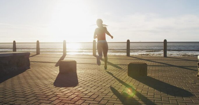 African american woman running on promenade by the sea at sundown
