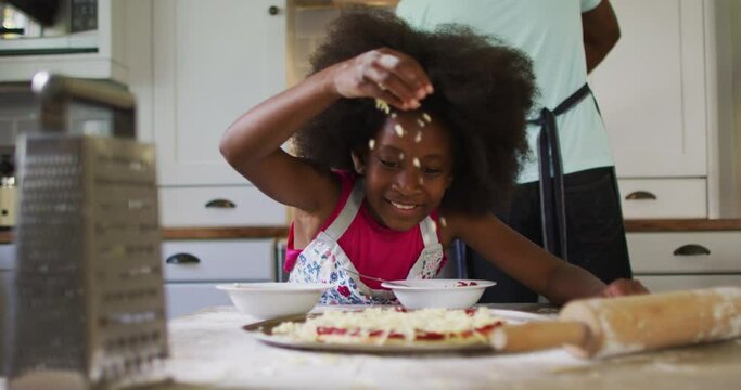 African american daughter making pizza in kitchen her father cooking in background