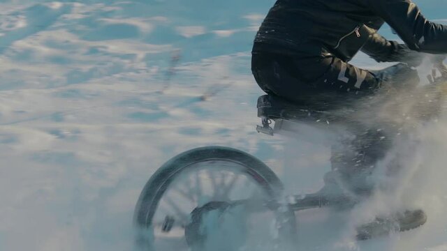 Cyclist in Black Clothes, Helmet and Snow Glasses Riding on Electric Bike in the Snow in Winter Forest. E-Bike Riding and Drifting at Cold Sunny Day - Slow Motion