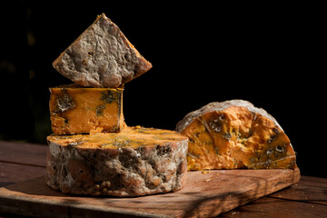 Still life of pile of shropshire blue cheese on a wooden board with a black back