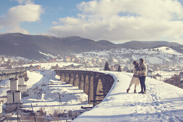 winter love story. guy and girl, man and woman in knitted sweaters walk on an old bridge in the mountains