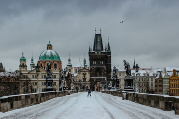 Obraz premium Winter view of Charles bridge, Old Town bridge tower covered with snow, Prague, Czech Republic. People walking through the city in the cold winter morning.Snowy day in town.Popular tourist destination