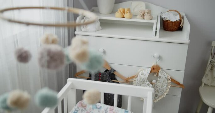 Handmade baby mobile toy hanging spinning above the crib in the bedroom. Close-up shot of multi colored nursery mobile in front of the baby changing table. Concept of childhood, new life, parenthood.
