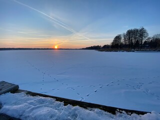 View of the frozen Białe lake near Włodawa with wooden platforms a lot of snow just before sunset elephant, orange sun like a falling comet golden hour