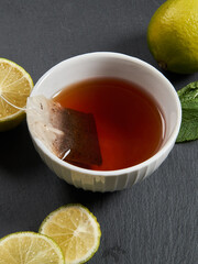 Tea in a white mug stands on a stone panel next to marshmallows and lime. There are pieces of spice for tea