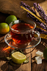 Tea in a white cup next to lime and flowers on a wooden background
