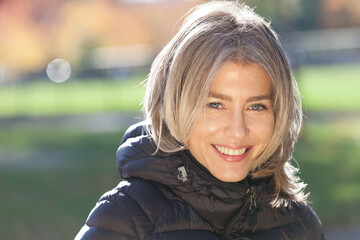 Portrait Of A Mature Woman Smiling At The Camera. Outside. Coat. Park.