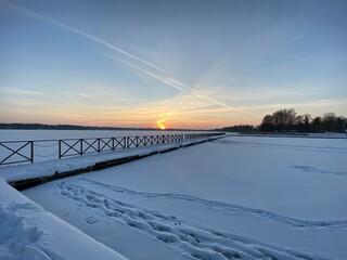 View of the frozen Białe lake near Włodawa with wooden platforms a lot of snow just before sunset elephant, orange sun like a falling comet golden hour © Józef