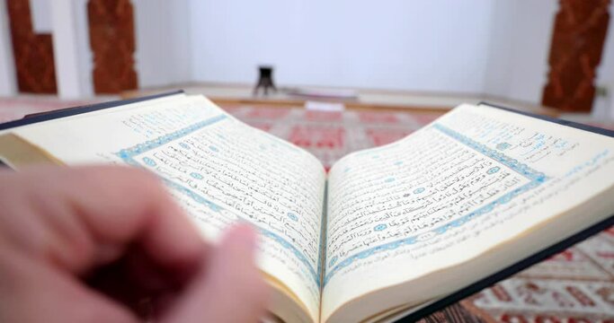 An opened Quran in a mosque lying on a Quran holder and a person leafing through the Quran