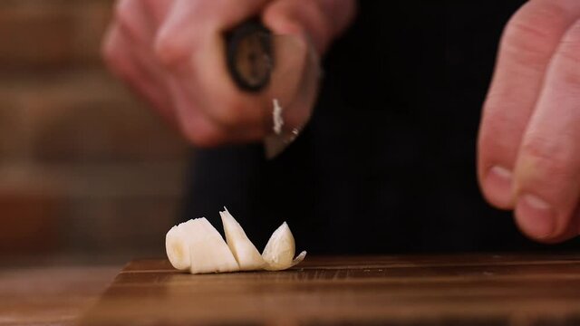 Chef slicing garlic cloves on a wooden board.