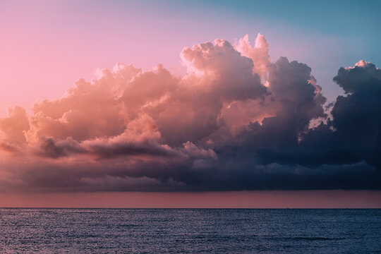 Cumulus dense clouds illuminated by the setting sun over the calm waters of the sea