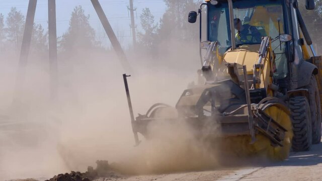 A wheeled tractor sweeps debris and dirt from the road with a rotating brush and kicks up a lot of dust around