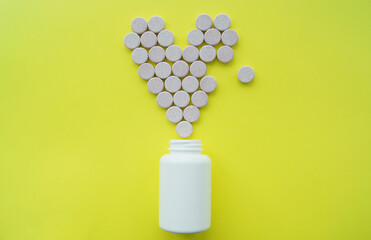 Flat lay of pink broken heart shape of medicine pills on yellow background. Concept of Valentine's Day or pharmacy, and day of Medical worker