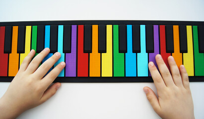 Hands of a child playing on a flexible multi-colored piano for children. Isolated on a white background