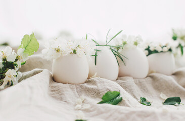 Fototapeta na wymiar Natural easter eggs in cute floral wreaths on linen fabric with blooming spring branch and petals