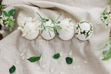Fototapeta na wymiar Happy Easter! Natural eggs in floral wreaths on linen fabric with blooming spring branch and petals