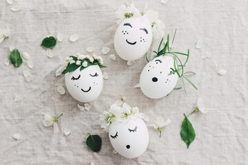Happy Easter! Natural eggs with drawn funny faces in cute floral crowns top view on linen fabric