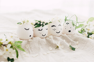 Natural easter eggs with drawn cute faces in floral wreaths on linen fabric with bloom in light