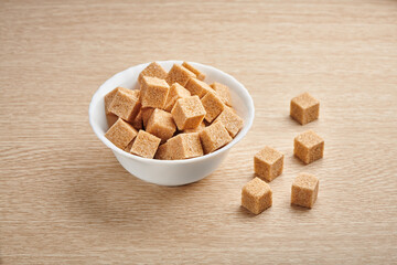 Heap of cubes of cane brown sugar in the bowl on the wooden kitchen table.