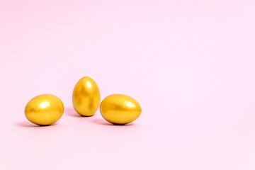Three Easter eggs decorated with gold paint on a pink background. Concept for Easter, spring. Selective focus. Copy space.
