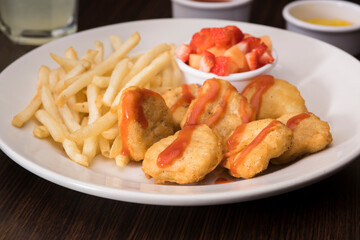 Plato de nuggets con ketchup, papas a la francesa y frutilla