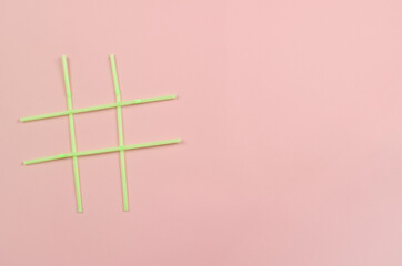 Hashtag symbol of green plastic beverage straws on pink background