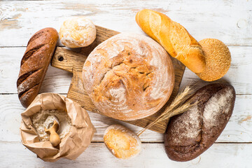 Assortment fresh bread and buns at white kitchen table.
