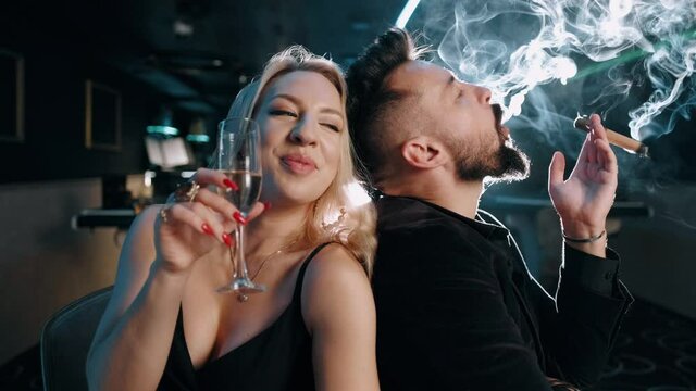 Portrait of an attractive business man and blonde woman. Bearded man with a cigar in a dark room. Rich successful people