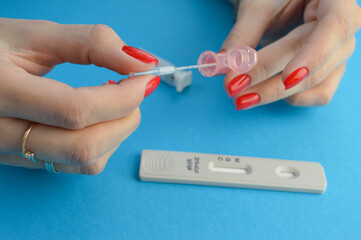a pink plastic container for blood collection. girl with red manicure collects liquid with a pipette to use the test. blood collection strip for coronavirus