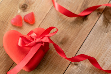 Closed red box in the shape of a heart with a red ribbon bow on wooden background with copy space. Photo of a gift box for Wedding, New Year, Christmas or Valentines Day. Top view. Close-up.