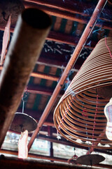 Asian circular burning incense spiral with red tassels hanging in temple in Hong Kong, China. Selective focus on burning incense.