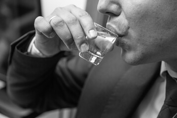 Closeup of male hand and lips while drinking glass of alcohol drink, made out of a Plum, a traditional Serbian Rakija drink.