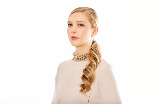 Studio portrait of pretty young woman wearing beige dress and stylish necklace