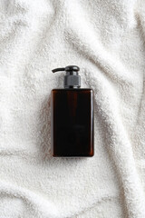 Amber glass pump shampoo bottle on white towel in bathroom. SPA natural organic cosmetics packaging design. Flat lay, top view.