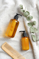 Hair care products, wooden comb and eucalyptus leaf on white towel. SPA natural organic cosmetics...