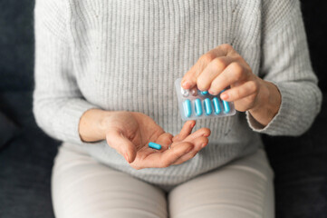 Top view of female hand holding a blue prescription pill and a blister pack, close-up of a palm of a senior lady with a tablet, taking medication or supplements for stronger immune system