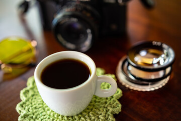 Xícara com café, câmera antiga e óculos com lentes amarelas sobre uma mesa de madeira.