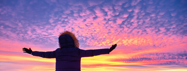 Fototapeta na wymiar Hiker girl in down jacket standing against amazing colorful sunset. Travel concept.